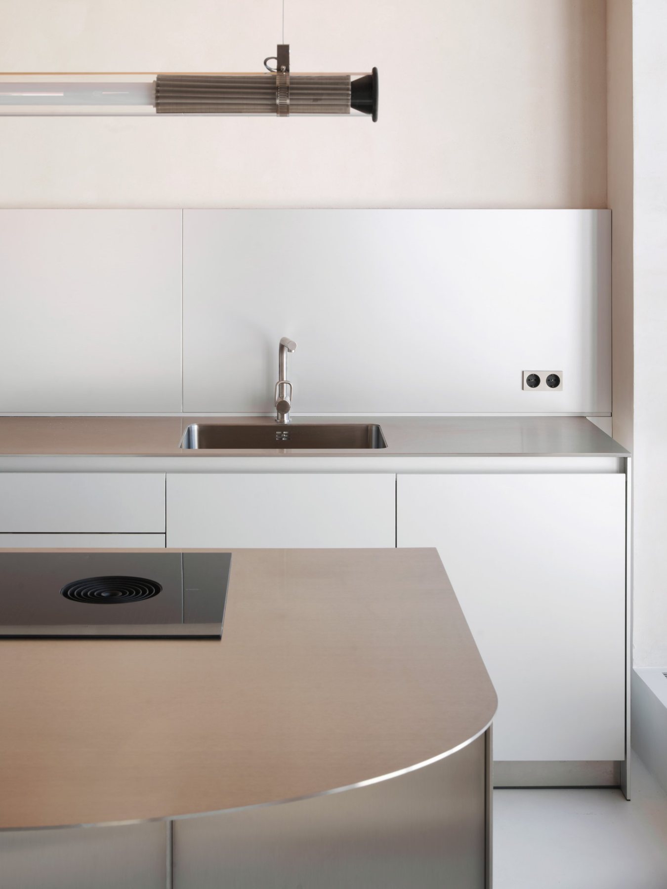 Soma House: cocina de acero inoxidable con isla de canto curvo